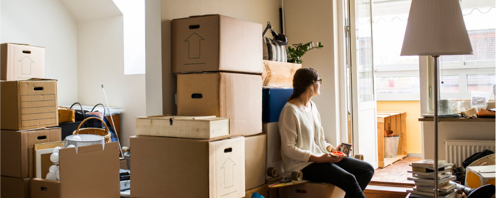 A woman sitting in a one bedroom flat with moving boxes around her